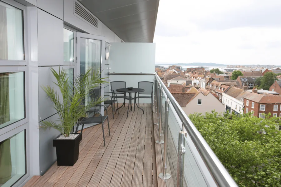 Schmaler Balkon mit Glasgeländer und Holzdielen mit Blick über die Stadt.