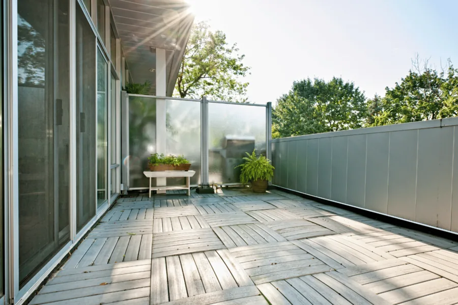 Balkon mit Milchglasgeländer und Holzdielen in der Nachmittagssonne.