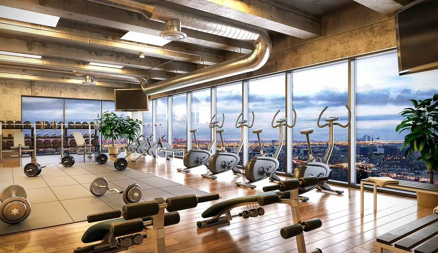 Fitnessraum mit Geräten entlang einer bodentiefen Fensterfront.