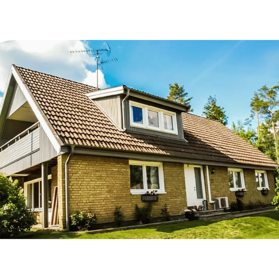 Ein gelbes Ziegelhaus mit braunem Dach, Gaubenfenstern, Terrasse und einer Satellitenschüssel auf dem Dach.