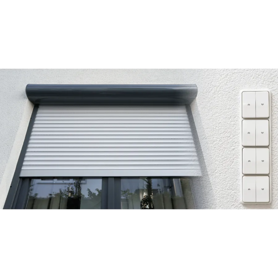 Graues Fenster mit Rollladen und vier Schaltern an einer weißen Wand.
