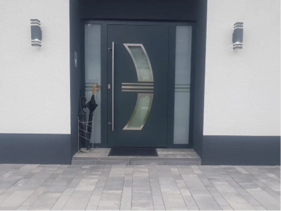 Anthrazitfarbene Haustür mit geschwungenem Glaseinsatz an einer hellen Fassade.