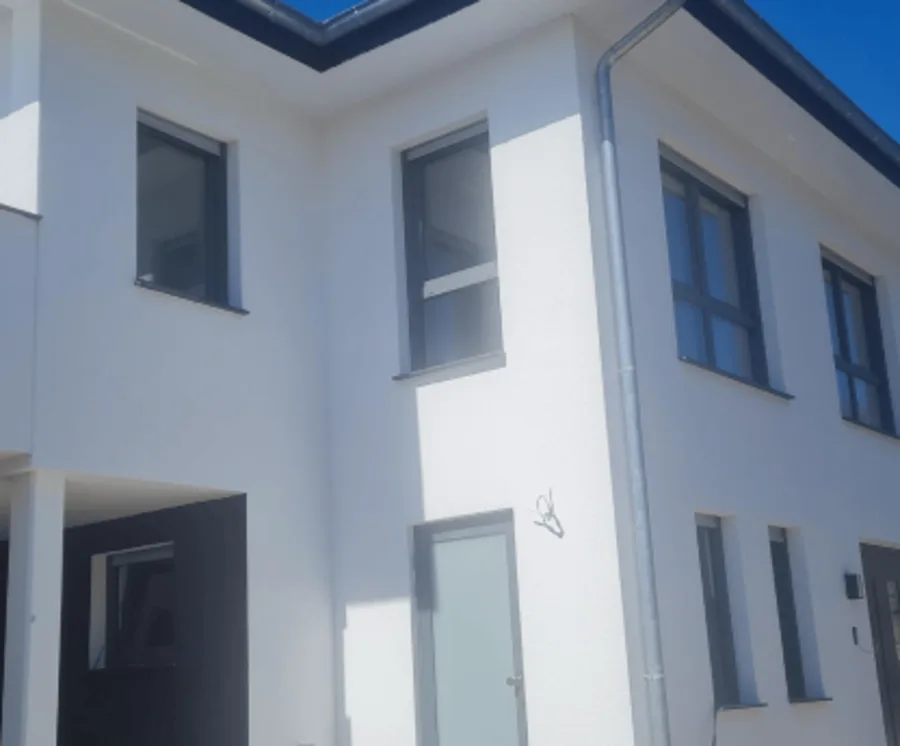 Weißes Wohnhaus mit anthrazitfarbenen Fenstern und Hauseingang.