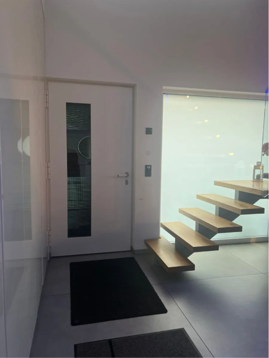 Heller Flur mit weißer Innentür und Blick auf eine freitragende Treppe.