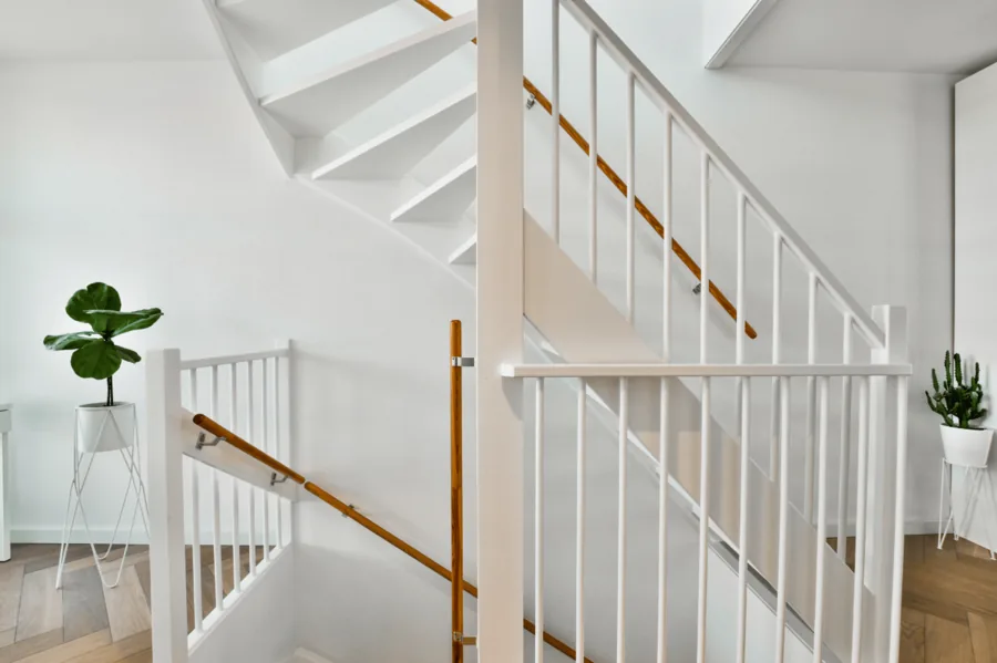 Treppenhaus mit weißen Stufen, Holzhandlauf und schlanken Geländerstäben.