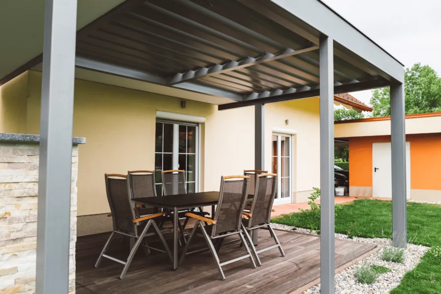 Terrassenüberdachung mit Lamellendach über Gartenmöbeln an einem Wohnhaus.