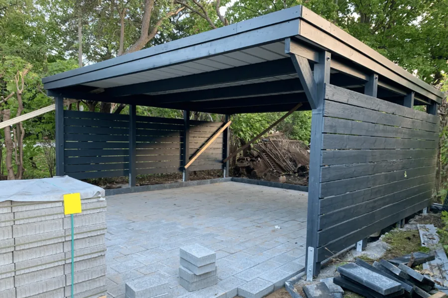 Carport im Bau mit dunkler Stahlkonstruktion und Holzverkleidung.
